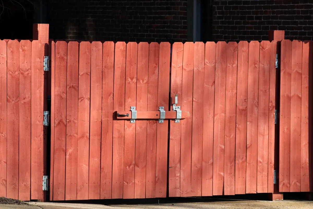 A rustic red wooden fence with a metal latch, highlighting the importance of secure fencing for repairs.